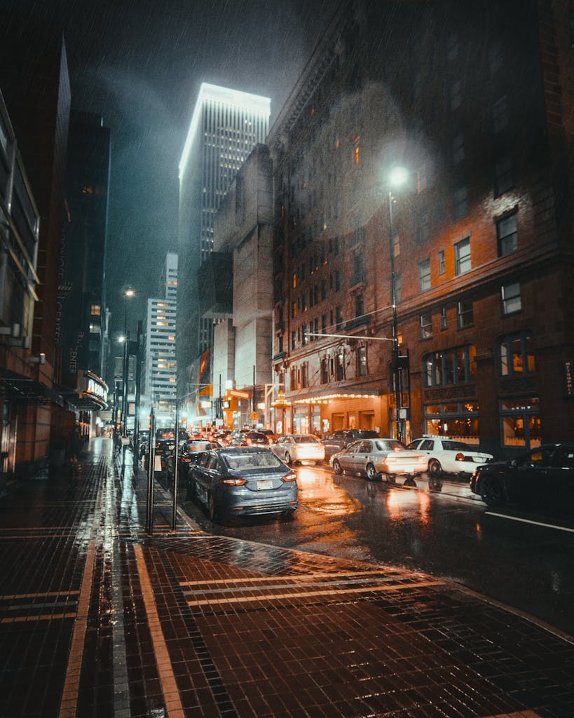 A dramatic view of a rainy night in Cincinnati's business district, showcasing urban architecture and traffic illuminated by city lights.