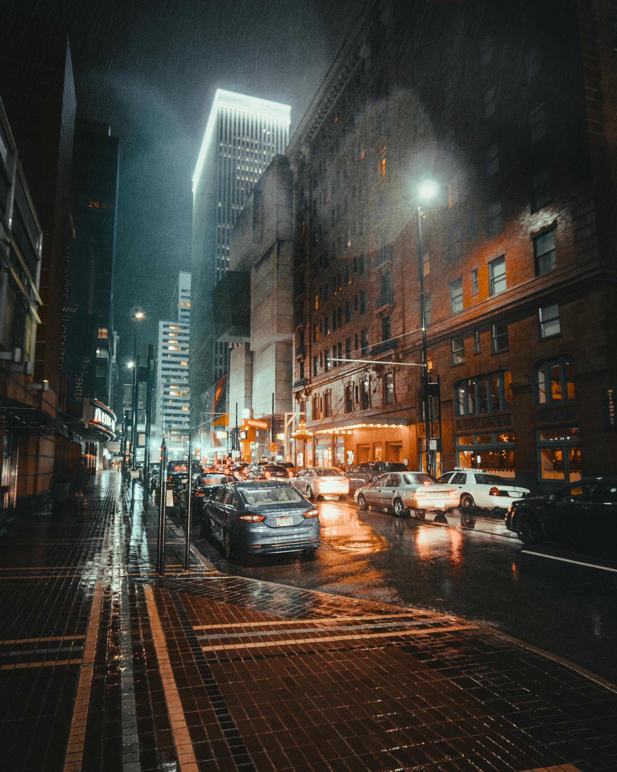 A dramatic view of a rainy night in Cincinnati's business district, showcasing urban architecture and traffic illuminated by city lights.